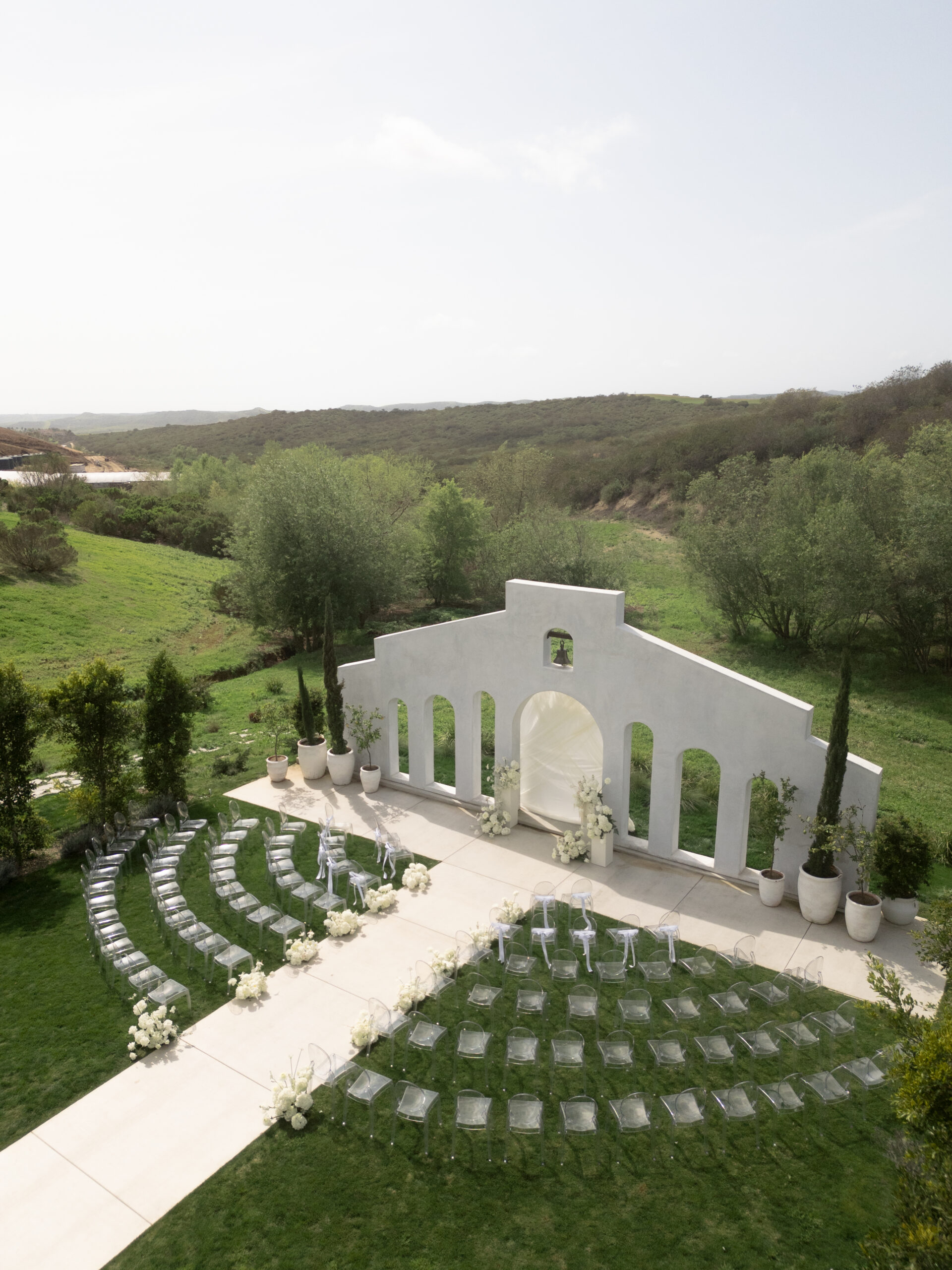 drone shot of Jeune Perche Ceremony site with white arch install and clear acryllic chairs arranged in arches